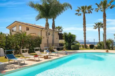 a pool with chairs and palm trees in front of a house at Panoramica Villa con Piscina sul Mare (Sanificata) in Cinisi
