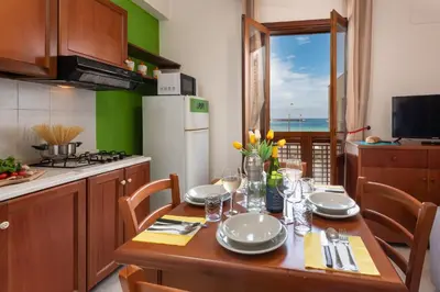 a kitchen with a wooden table with chairs and a refrigerator at I Tre Golfi Beach Apartments in San Vito lo Capo