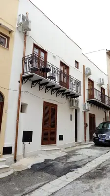 a white building with balconies and a car parked in front at Monolocali Leonardo in Castellammare del Golfo