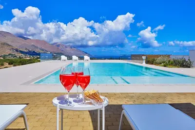 two glasses of wine on a table next to a swimming pool at Villa Etesiae in Castellammare del Golfo