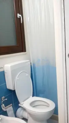 a bathroom with a white toilet and a blue shower curtain at Charming House in Castellammare del Golfo with Balcony in Castellammare del Golfo