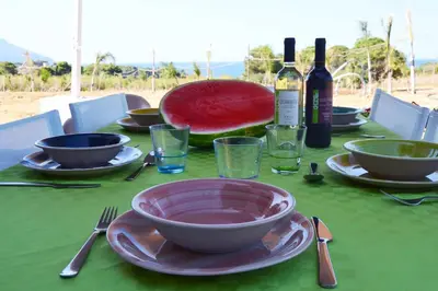 a table with a plate of watermelon and wine bottles at Splendida Villa NATURE-APPARTAMENTO MELOGRANO a SCOPELLO-ZINGARO vista sul mare in Scopello