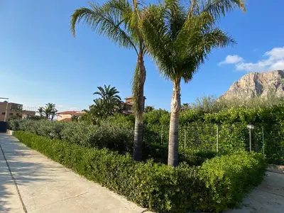 two palm trees and a fence with a mountain in the background at Villa Marcione Garden & House in Cinisi