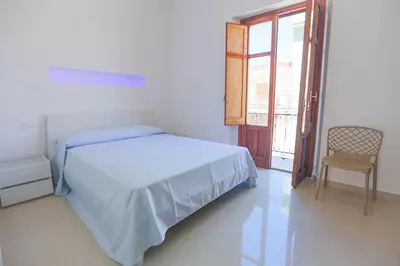 a white bedroom with a bed and a chair at Casa in centro in Castellammare del Golfo