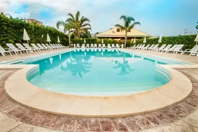 a large swimming pool with chairs and a resort at Case Vacanze Paradise Beach Vicino Cefalù PISCINA APERTA in Campofelice di Roccella