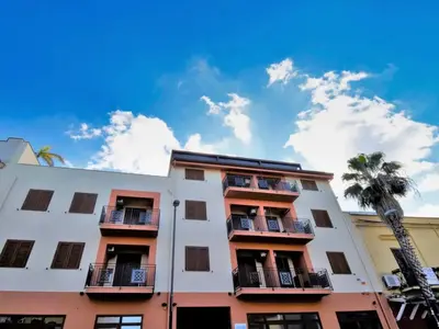 a white building with balconies and a palm tree at Azzurra Apartments in Balestrate