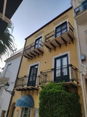 a yellow building with black balconies and a tree at la palma in Castellammare del Golfo