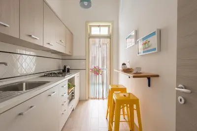 a kitchen with white cabinets and a sink and two stools at Vento di Grecale - a pochi metri dal mare in Santa Flavia