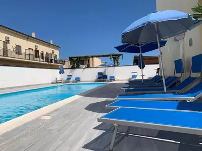 a swimming pool with blue chairs and an umbrella at Casa Vacanze Costanza in San Vito lo Capo