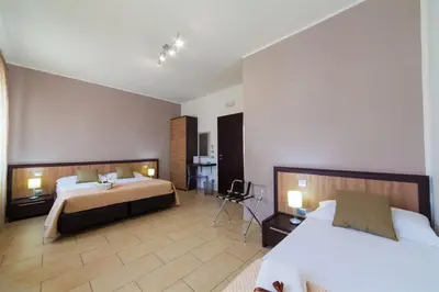 a hotel room with two beds and a chair at Kristal in San Vito lo Capo