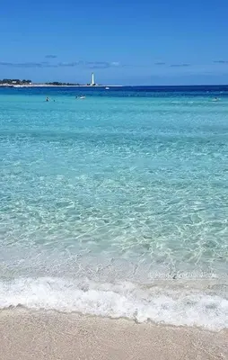 a beach with blue water and a lighthouse in the background at Alofara Apartment in San Vito lo Capo