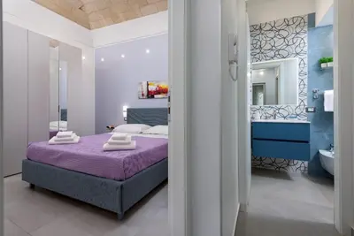 a bedroom with a purple bed and a bathroom at Alofara Apartment in San Vito lo Capo