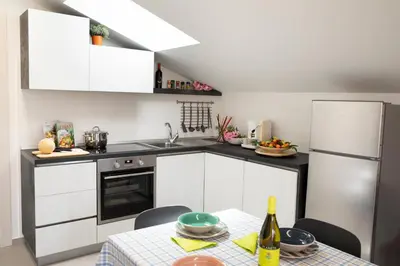 a kitchen with white cabinets and a table and a refrigerator at Appartamenti in Villa Nature con vista mare e monti in Scopello