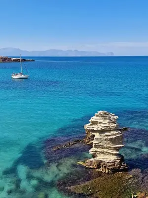 a rock formation in the water with a sail boat at Casa Melf in Terrasini