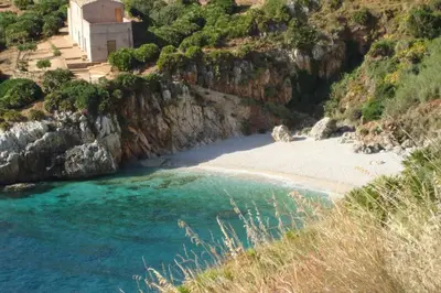 a beach with a church on the side of a mountain at La Palma in San Vito lo Capo