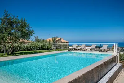 a swimming pool with chairs and the ocean in the background at Villa Maria con piscina e vista mare in Castellammare del Golfo