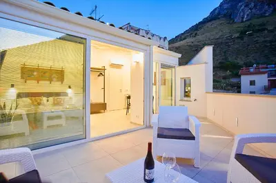 a patio with white chairs and a table with a bottle of wine at Porta del Golfo Apartments & Suites in Castellammare del Golfo