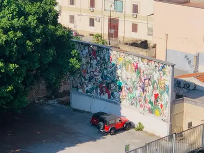 a red car parked in front of a wall with a mural at Sostegno d'amore in Palermo