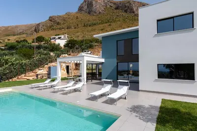 a house with a swimming pool with white chairs at Villa vista mare con piscina a sfioro a Scopello in Castellammare del Golfo