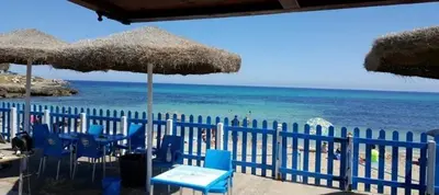 a beach with blue chairs and umbrellas and the ocean at B&B Torre Pozzillo in Cinisi