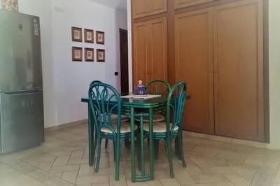 a green dining room table with four chairs and a refrigerator at Casa del Grecale in Isola delle Femmine