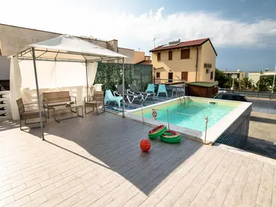 a swimming pool with a table and chairs and an umbrella at Seafront Apartment in Villa with Swimming Pool and Parking in Alcamo Marina