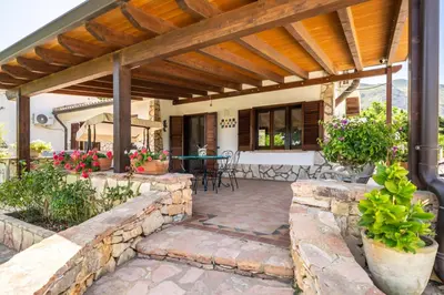 an outdoor patio with a stone wall and a wooden pergola at VILLA HIBISCUS in Castellammare del Golfo