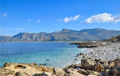 a rocky beach with mountains in the background at Pietro 2 in San Vito lo Capo