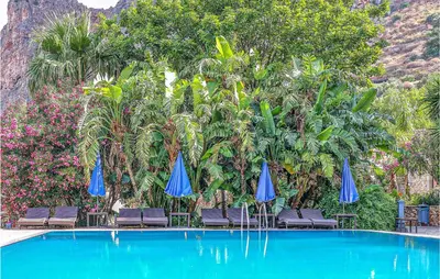 a pool with blue umbrellas and chairs and palm trees at Pietro 2 in San Vito lo Capo
