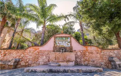a fountain in front of a stone wall with palm trees at Pietro 3 in San Vito lo Capo