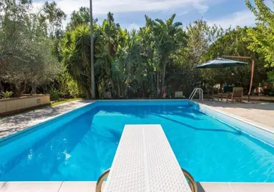 a blue swimming pool with a table and an umbrella at Villa Flora in Castellammare del Golfo