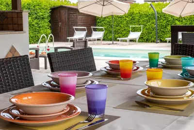 a table with plates and bowls and glasses next to a pool at Deluxe Sicily Villa in Buonfornello