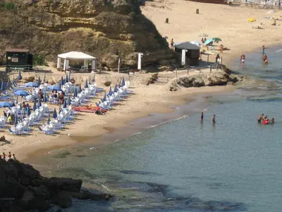 a beach with a bunch of chairs and people in the water at Charmrooms in Castellammare del Golfo