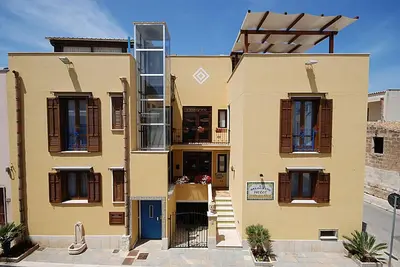 a yellow building with brown shuttered windows at Hotel Il Melograno in San Vito lo Capo