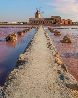 a pathway in the water with a windmill in the background at A-marè - CasaVacanza in Trappeto