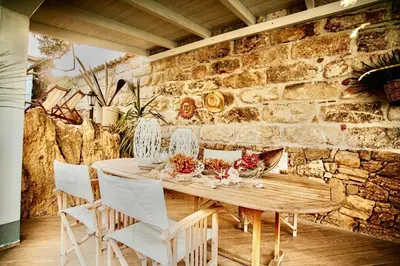 a wooden table with white chairs and a stone wall at Villa Dorotea con piscina in Trappeto