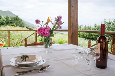 a table with a bottle of wine and a vase of flowers at VILLA BIFAMILIARE SCOPELLO in Scopello
