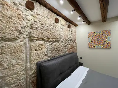 a bedroom with a stone wall with a black leather bed at Tommy's rooms in Palermo