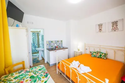 a small bedroom with an orange bed and a kitchen at Cà del Re Holiday in Partinico