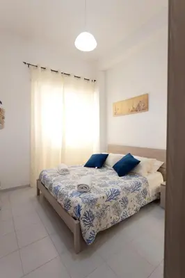 a bedroom with a bed with blue pillows and a window at Confortevole appartamentino in Castellammare del Golfo
