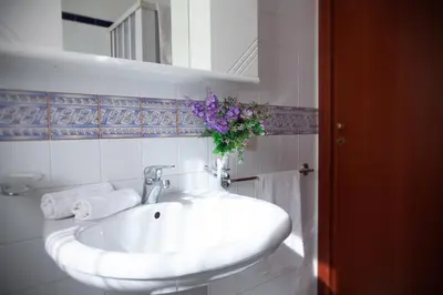 a white bathroom sink with a vase of purple flowers at Case Vacanza Sabbia Rosa in San Vito lo Capo