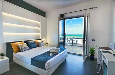 a bedroom with a bed and a balcony with the ocean at Hotel La Battigia in Alcamo Marina