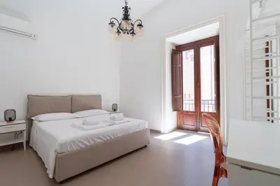 a white bedroom with a bed and a chandelier at Quattro Canti by DomuSicily in Palermo