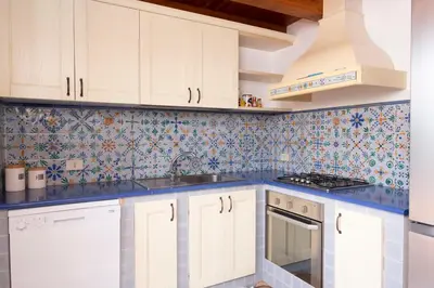 a kitchen with white cabinets and blue tiles on the wall at Villa Morici con ampio giardino in San Vito lo Capo