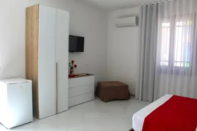 a white bedroom with a bed and a cabinet and a window at B&B La CYCAS in San Vito lo Capo