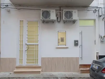 a white house with two windows and a door at Airport Home TUREI & BRINGO Car Rental in Cinisi