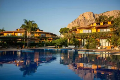 a resort with a pool and mountains in the background at Magaggiari Hotel Resort in Cinisi