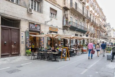 people walking down a street with tables and chairs and umbrellas at Casa dei Quattro Canti B&B in Palermo