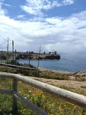 a fence and the ocean with a castle in the distance at Sea life Terrasini in Terrasini