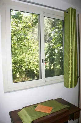 a window with green curtains and a wooden table at Camera indipendente con bagno immersa nel verde in Bagheria
